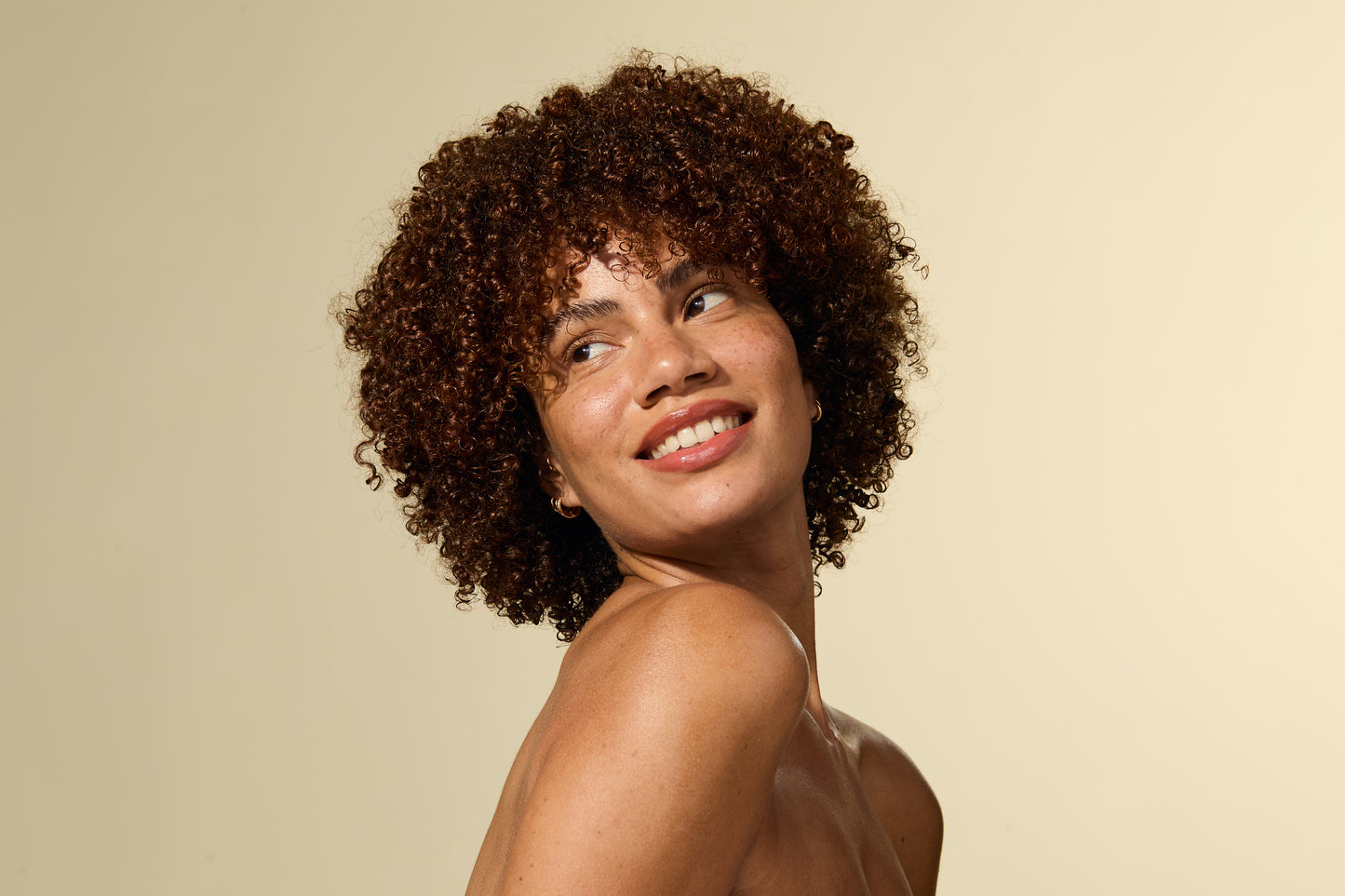 Woman with curly hair smiling against a beige background