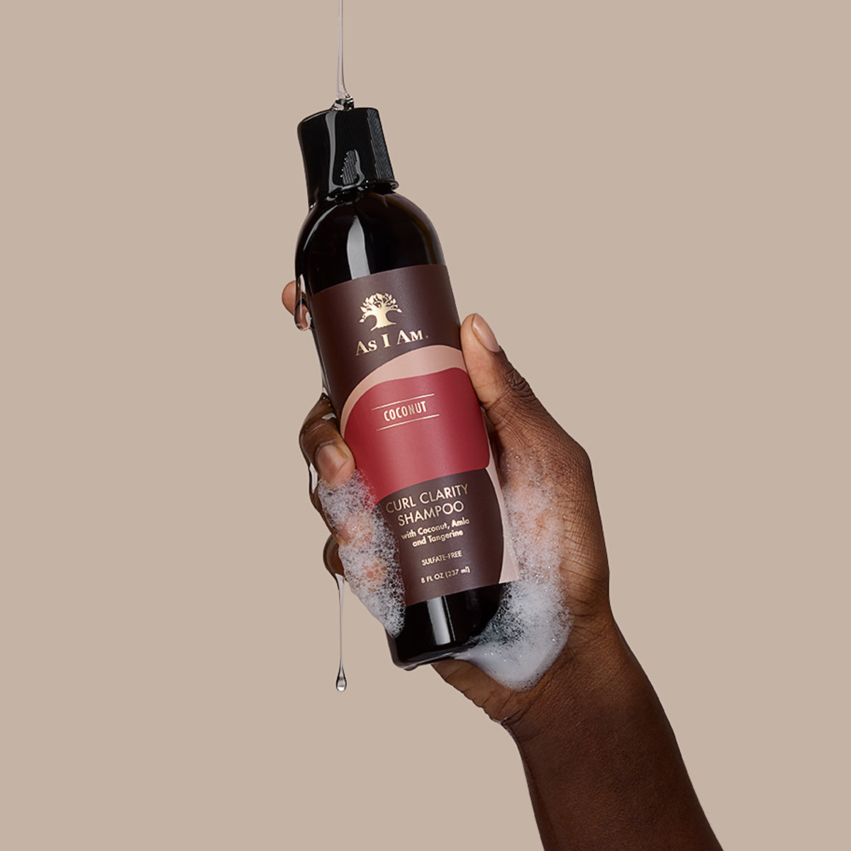 Hand holding a bottle of 'As I Am' shampoo with a beige background