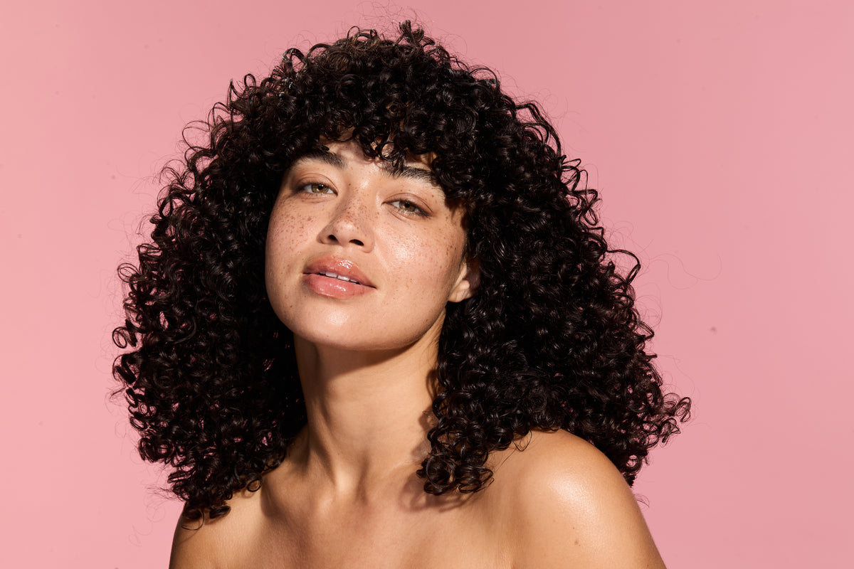 Woman with curly hair against a pink background