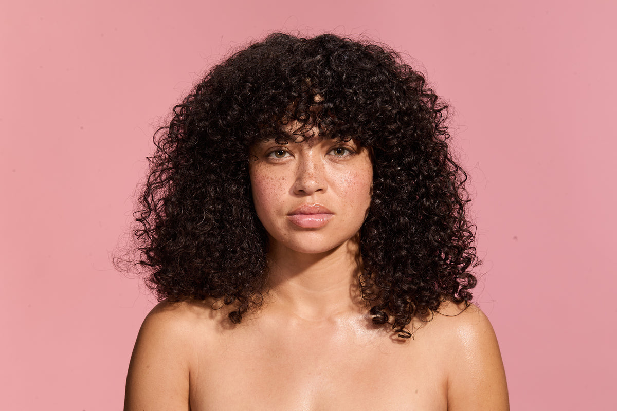 Woman with curly hair against a pink background