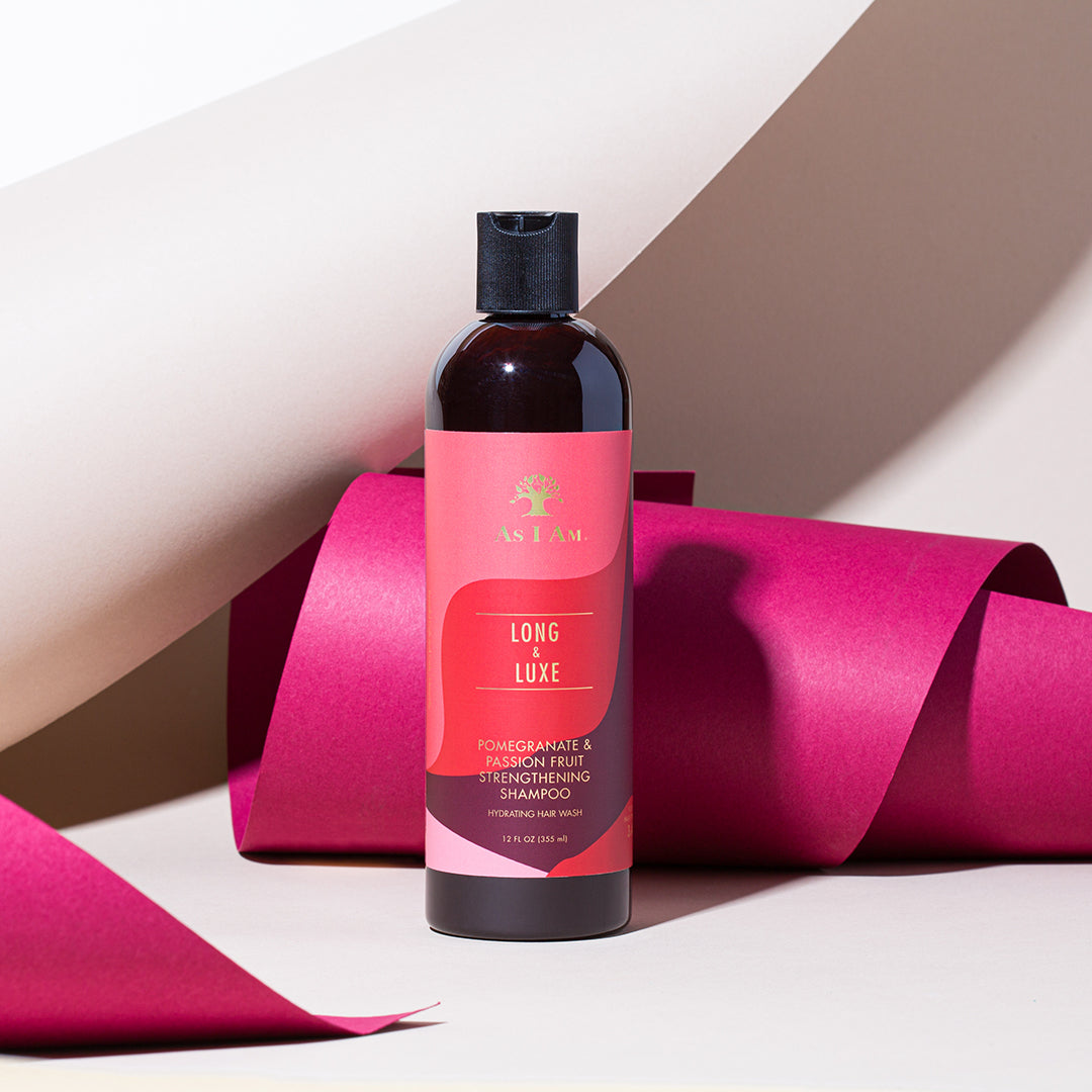 A bottle of Long & Luxe Strengthening Shampoo with a pink and orange label, presented with pink ribbons in the background.