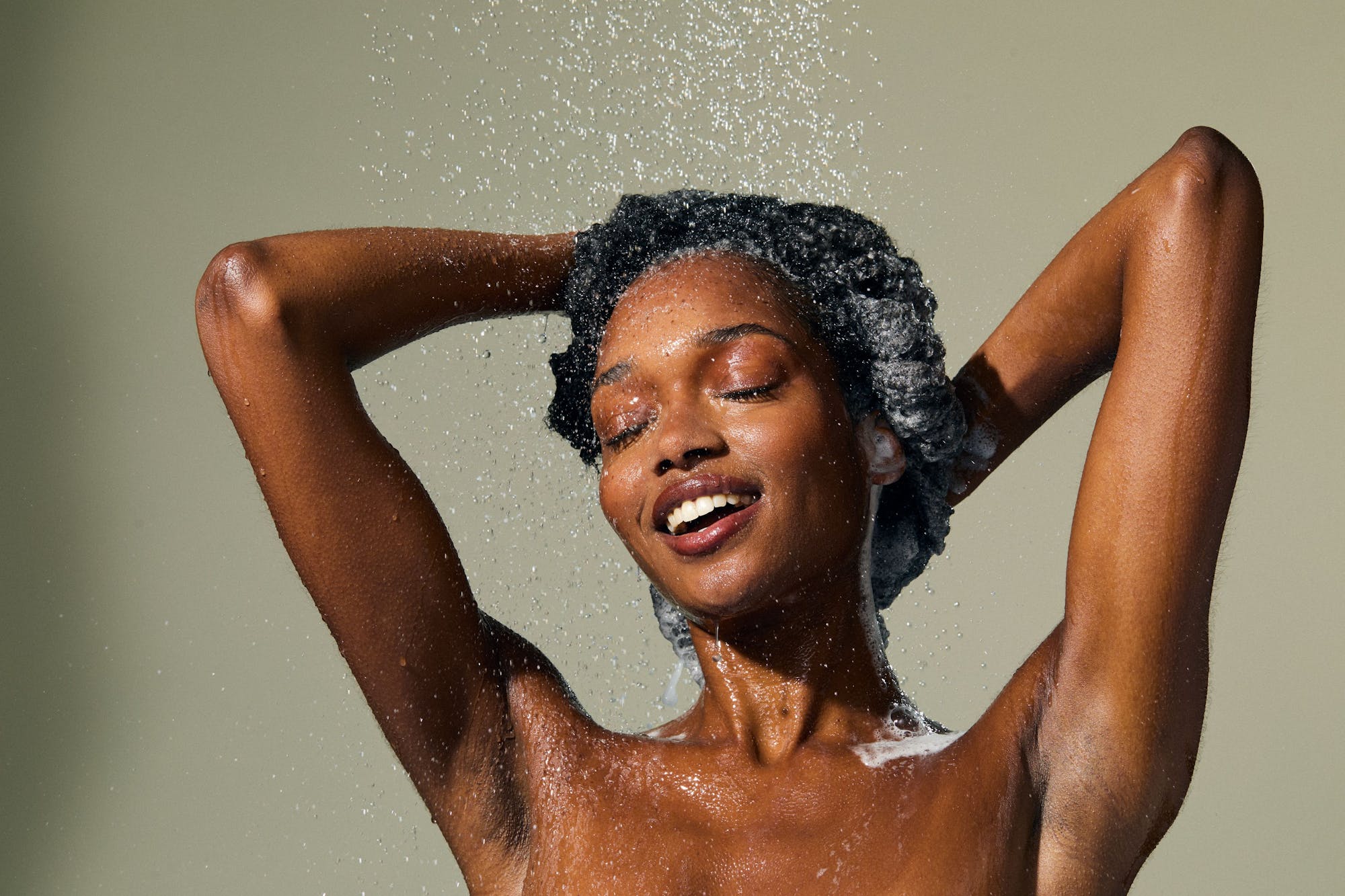 Woman with wet hair under a shower with a neutral background