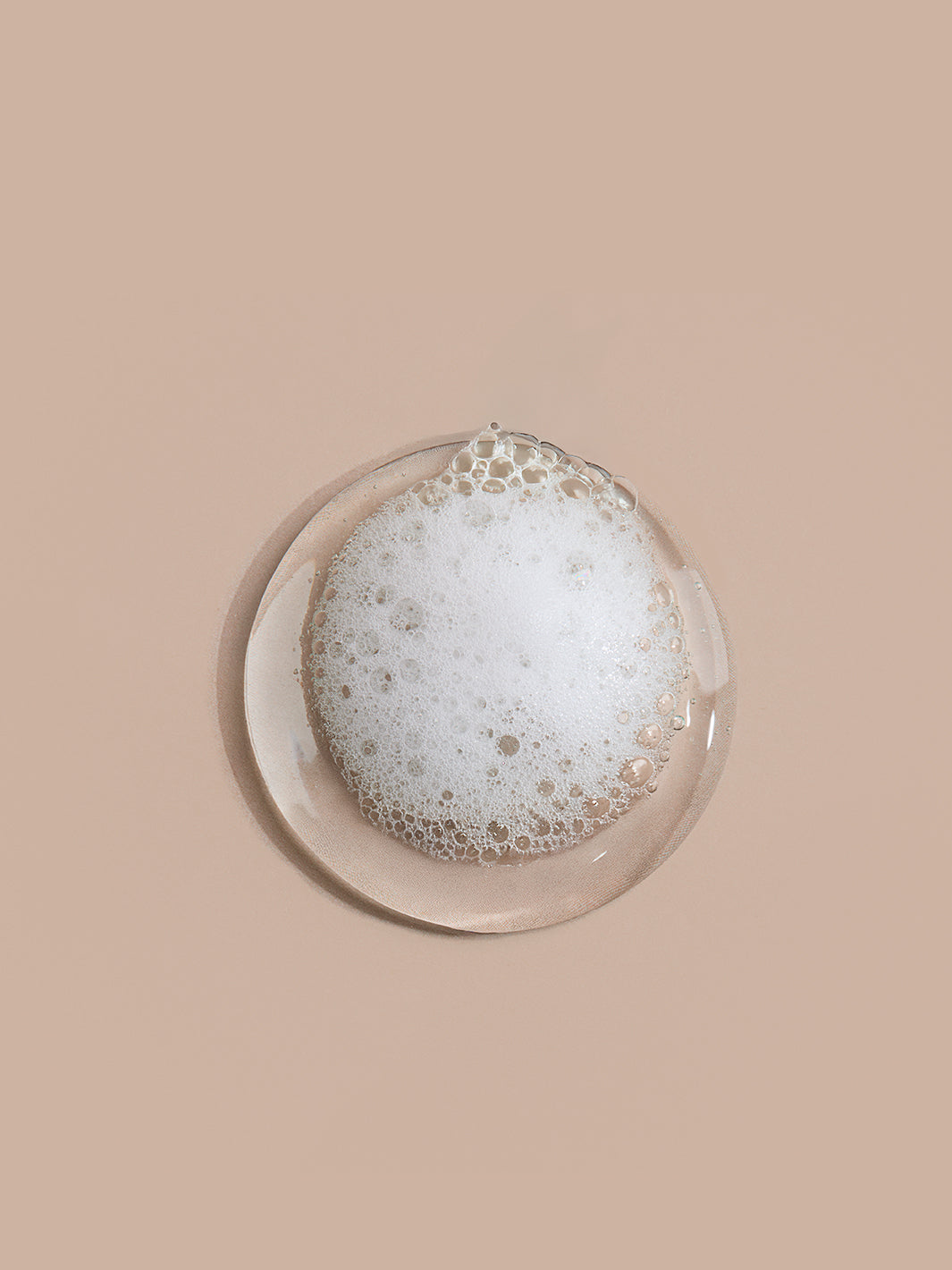 Round glass dish with soapy bubbles on a beige background