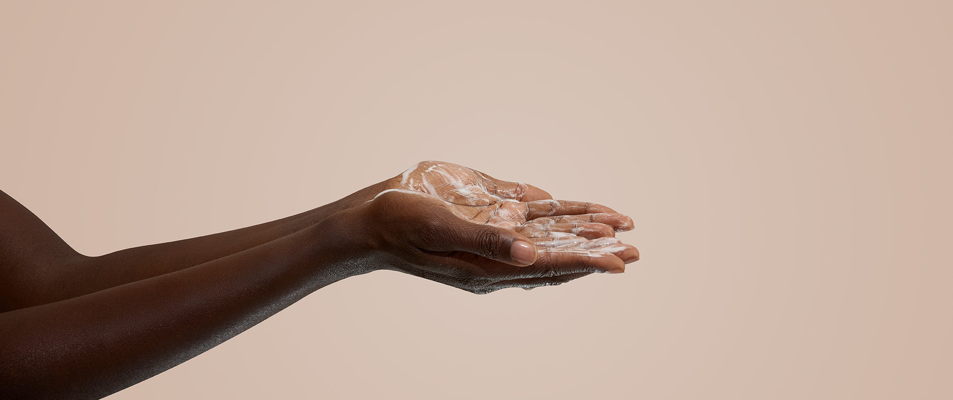 Hand holding a small amount of cream against a beige background
