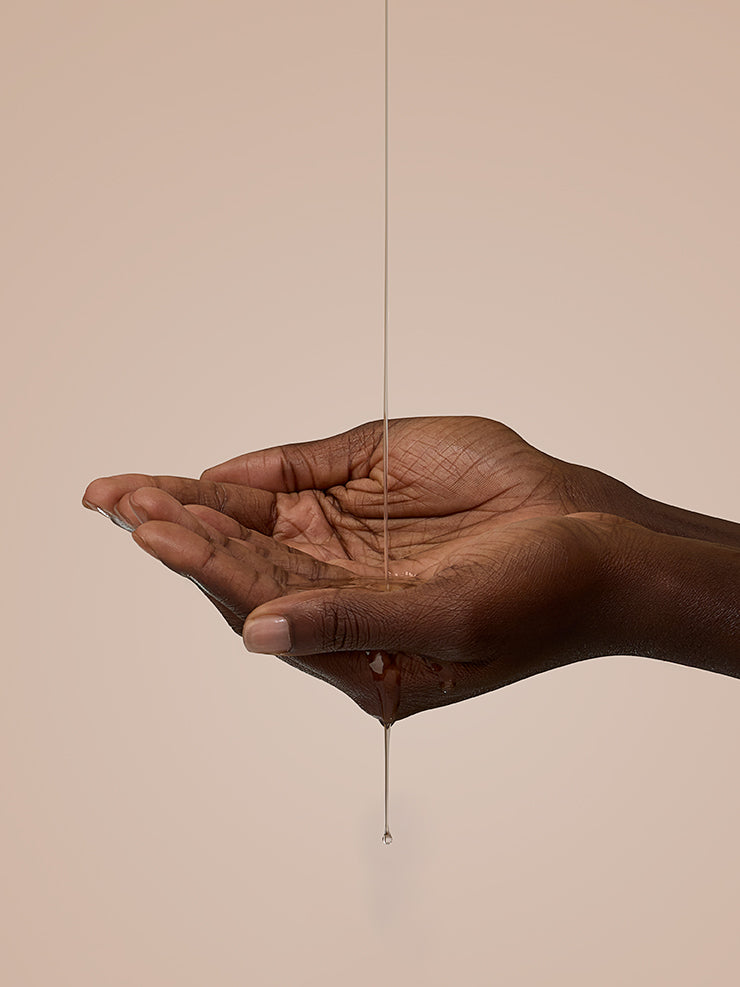Hand holding a dangling gold earring against a beige background