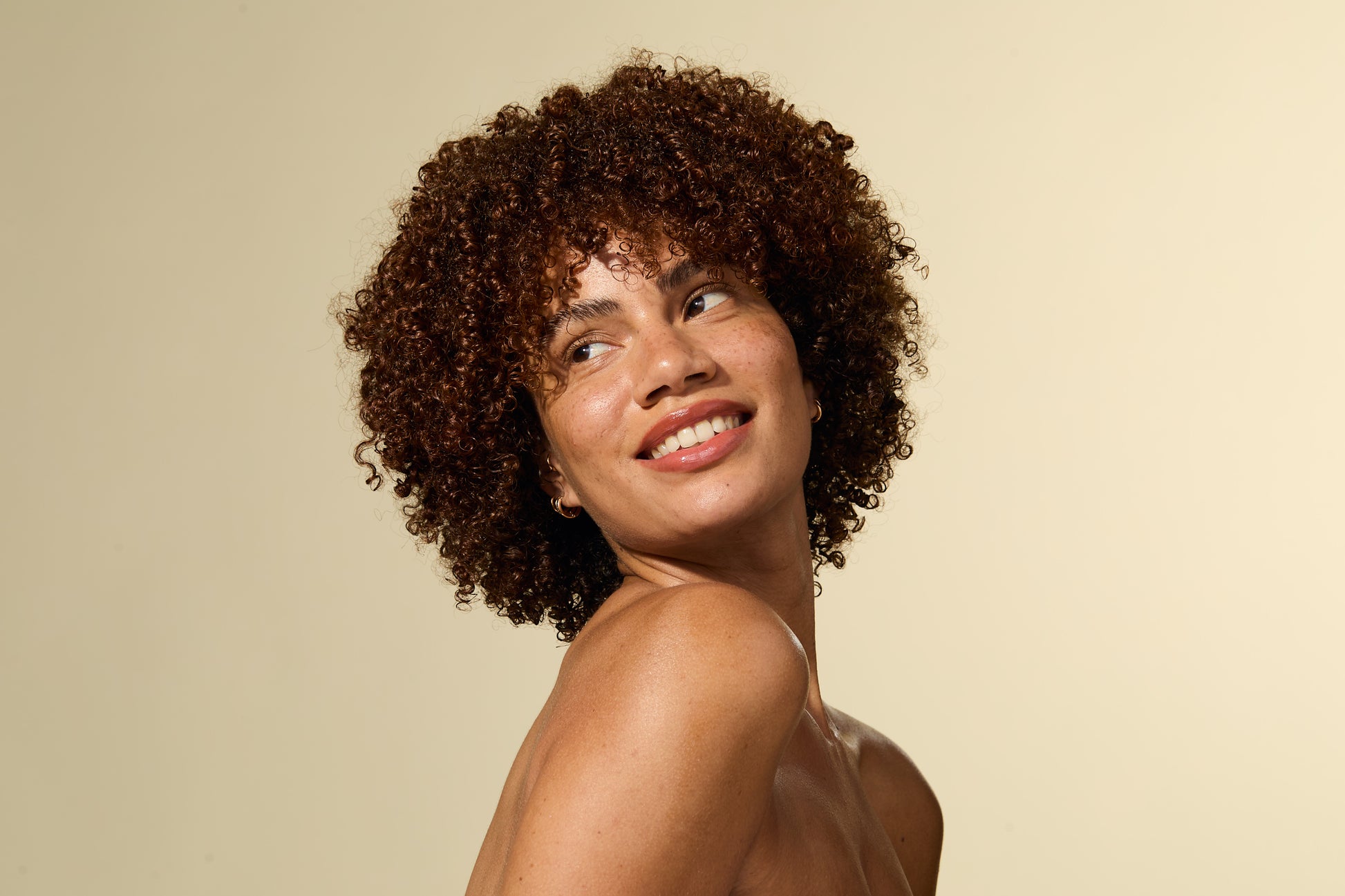 Woman with curly hair smiling against a beige background