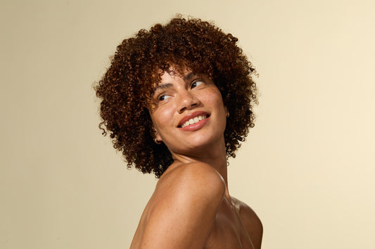 Woman with curly hair smiling against a beige background