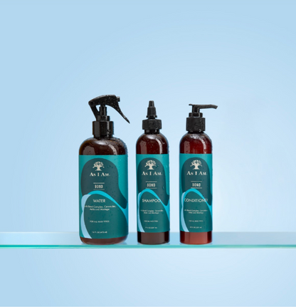 Three bottles of 'As I Am' hair care products on a clear surface with a light blue background
