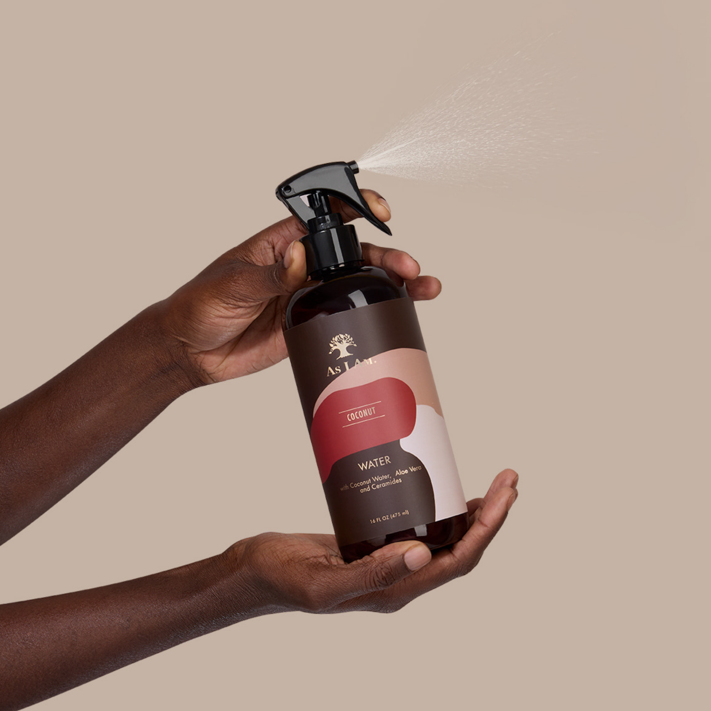 Hand holding a brown spray bottle with a visible brand logo against a beige background