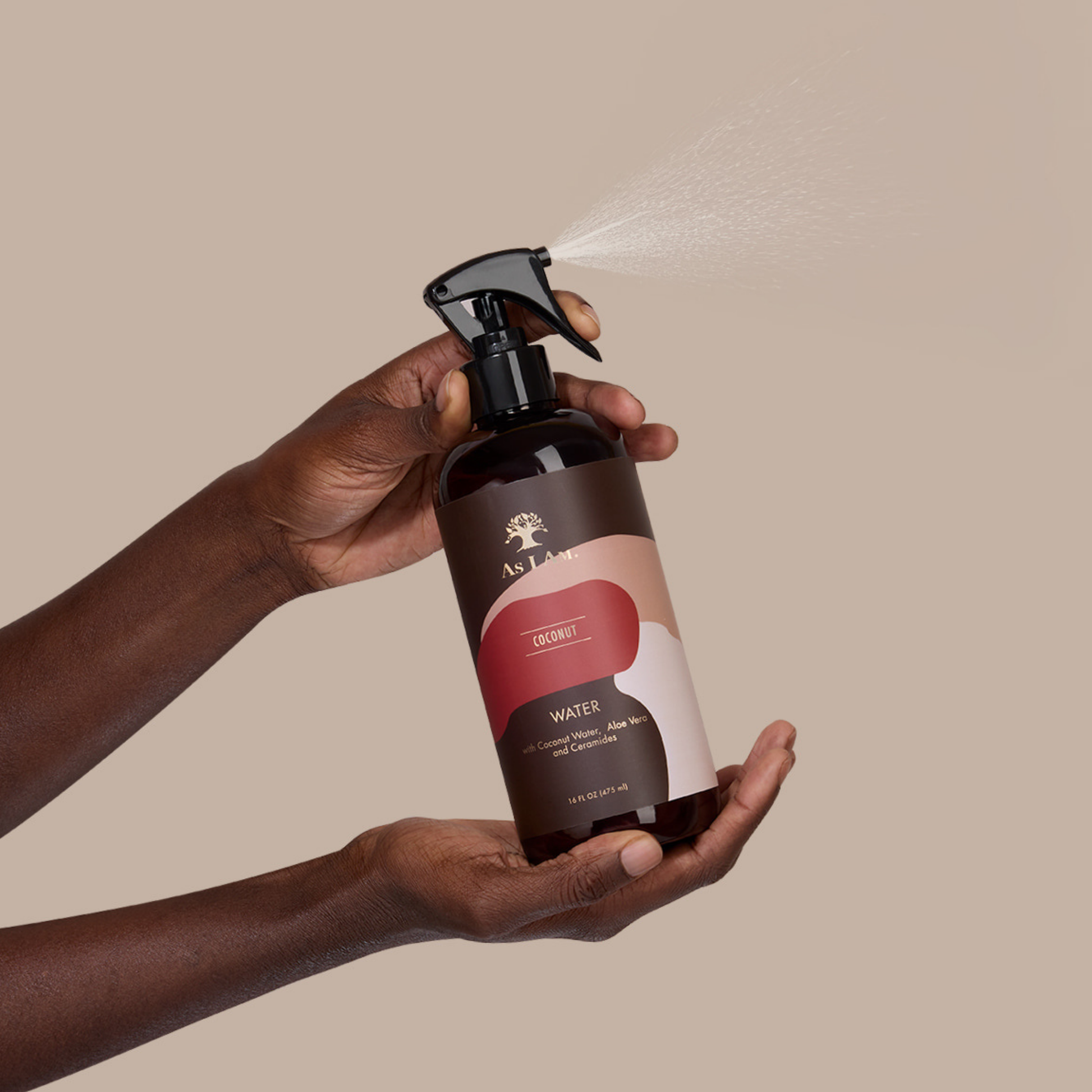Hand holding a brown spray bottle with a visible brand logo against a beige background