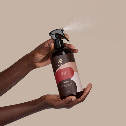 Hand holding a brown spray bottle with a visible brand logo against a beige background