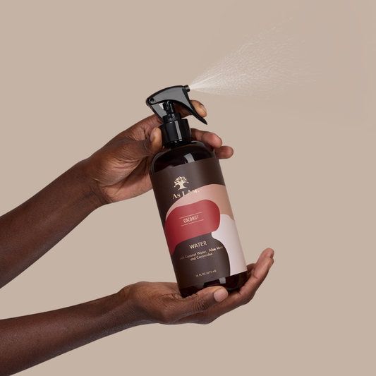 Hand holding a brown spray bottle with a visible brand logo against a beige background