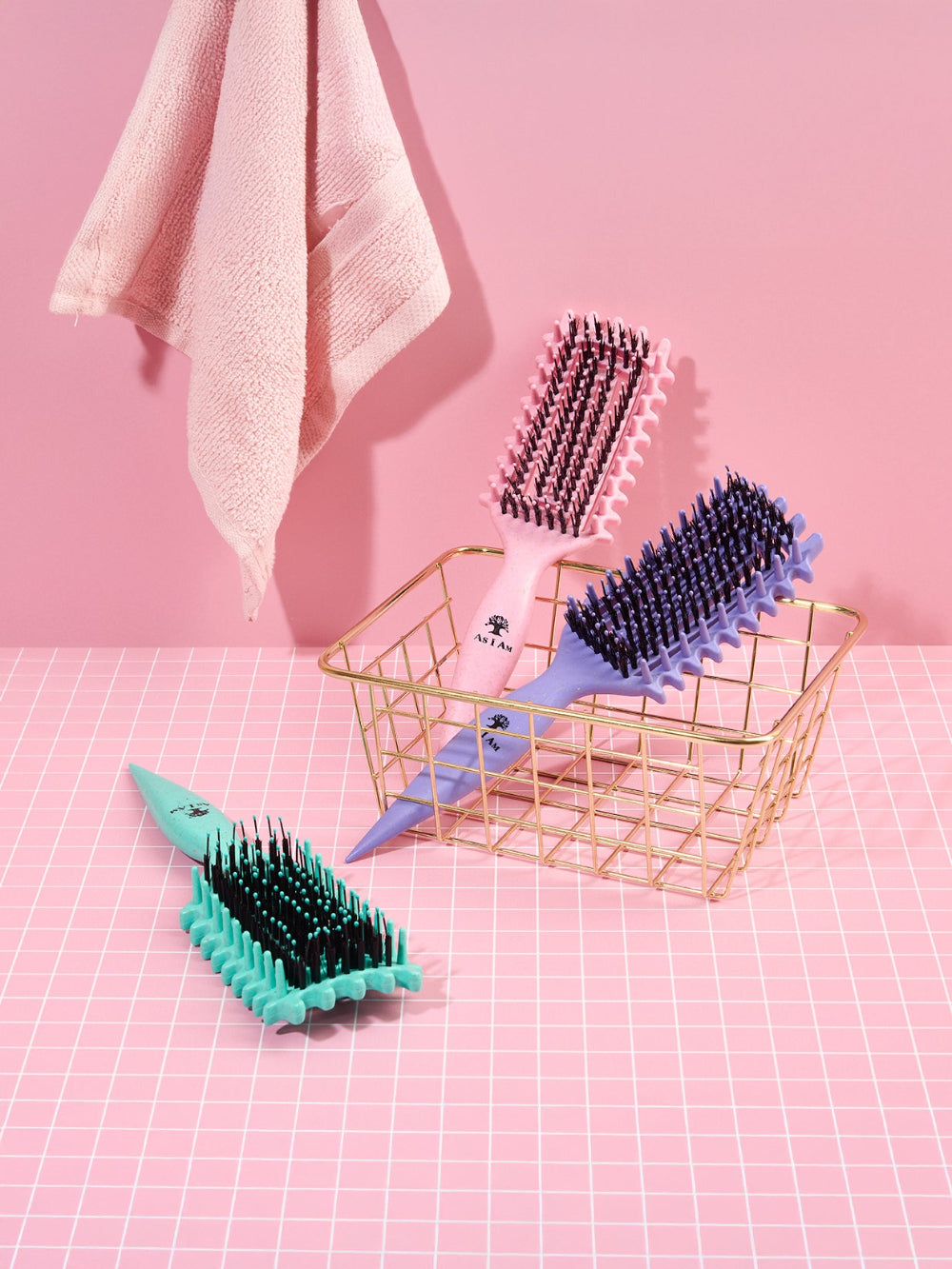 Three hairbrushes in different colors on a pink grid background with a gold basket.