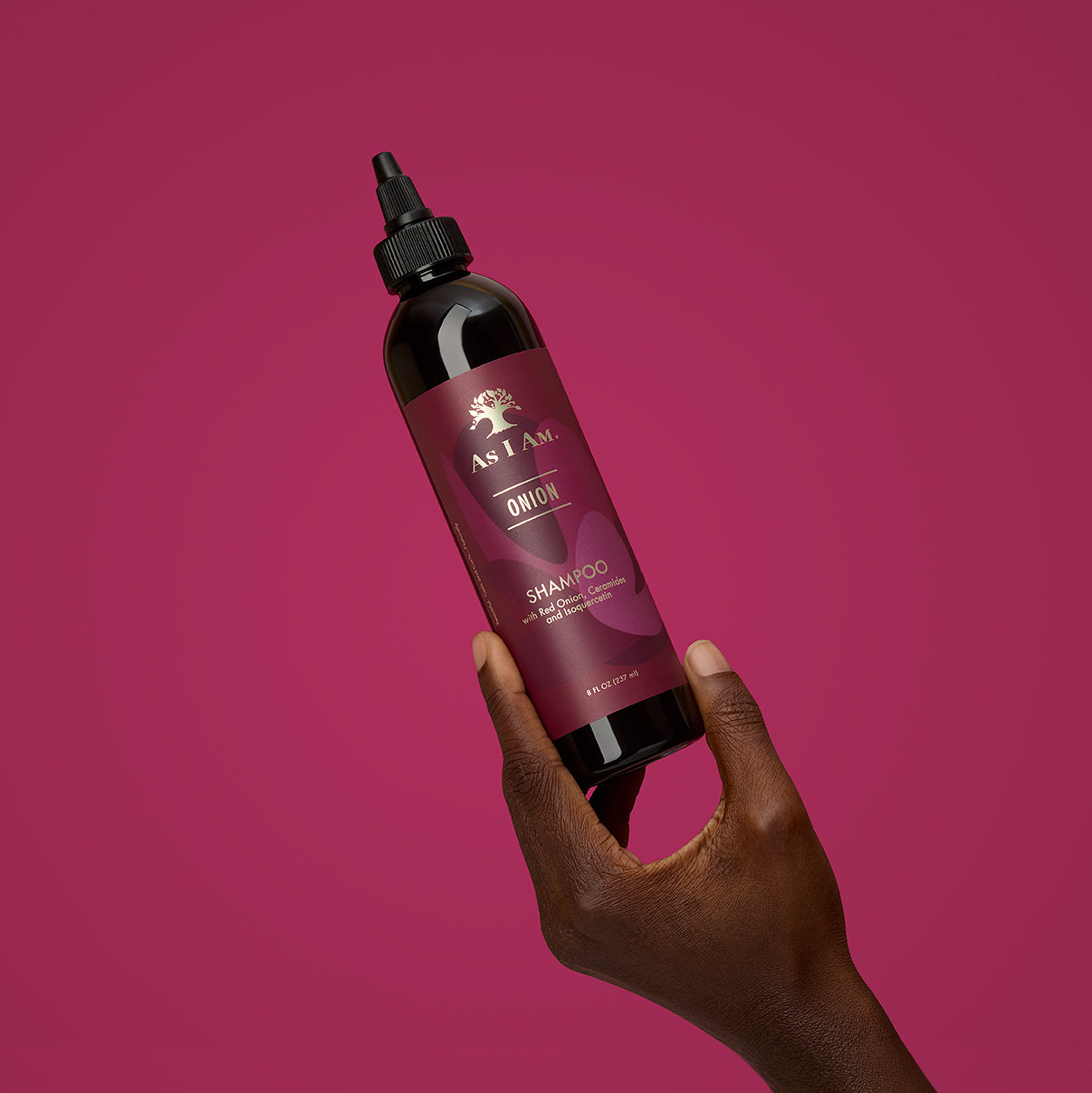 Hand holding a bottle of As I Am Onion Shampoo against a pink background