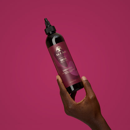 Hand holding a bottle of As I Am Onion Shampoo against a pink background