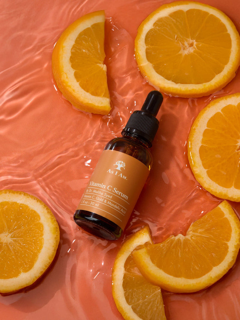 Bottle of serum with dropper surrounded by sliced oranges on a pink background
