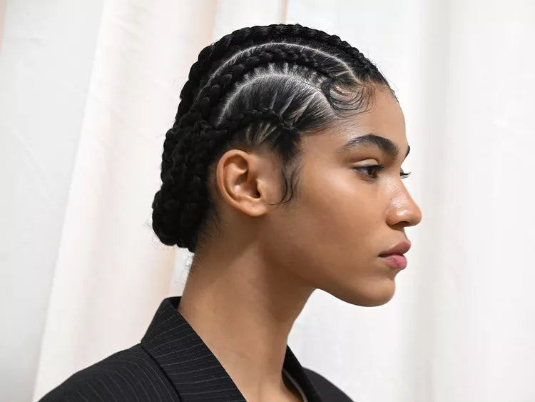 Woman with braided hair wearing a black outfit against a white curtain background