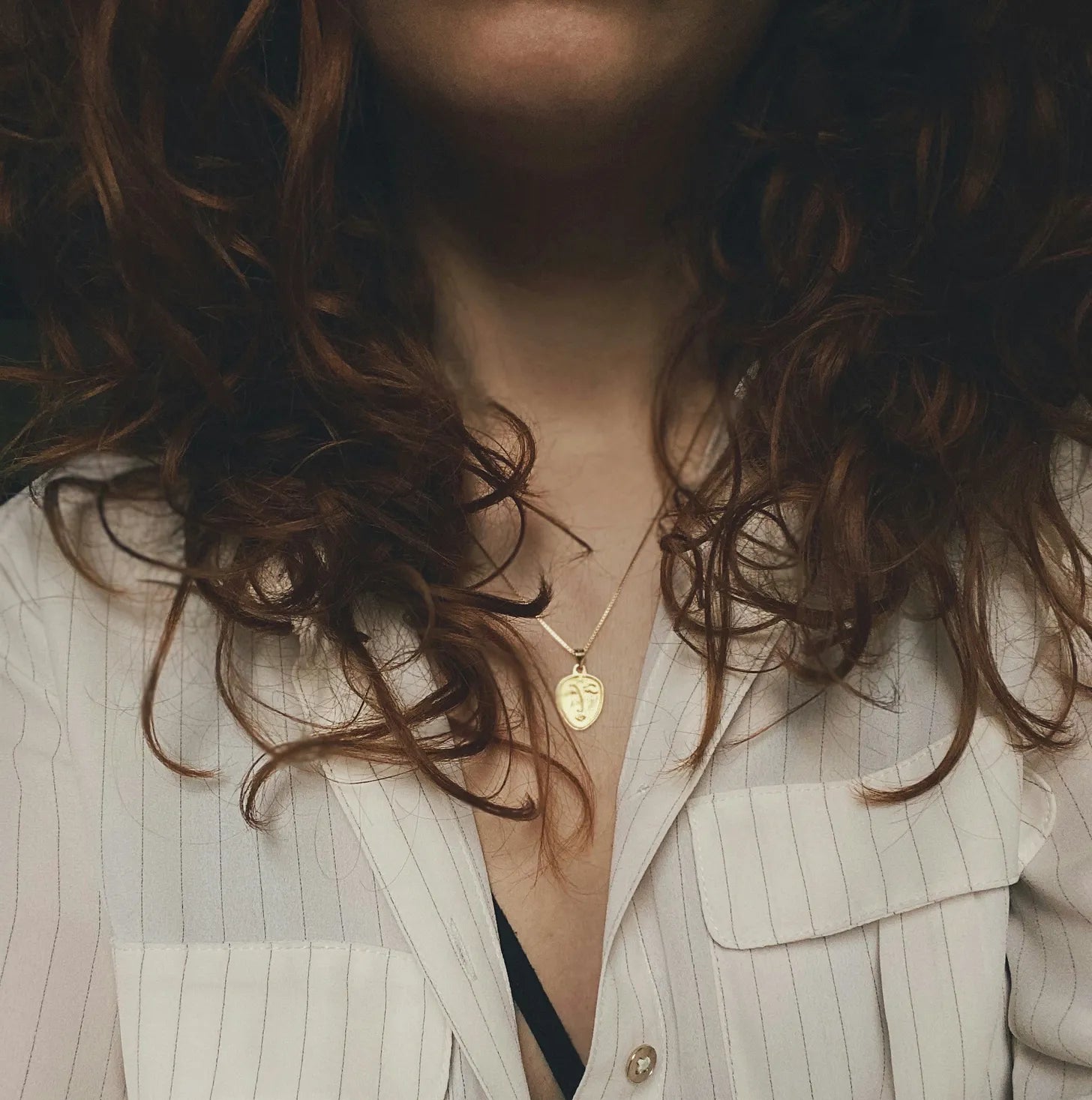 Close-up of a person wearing a gold necklace with a pendant, partially obscured by hair.