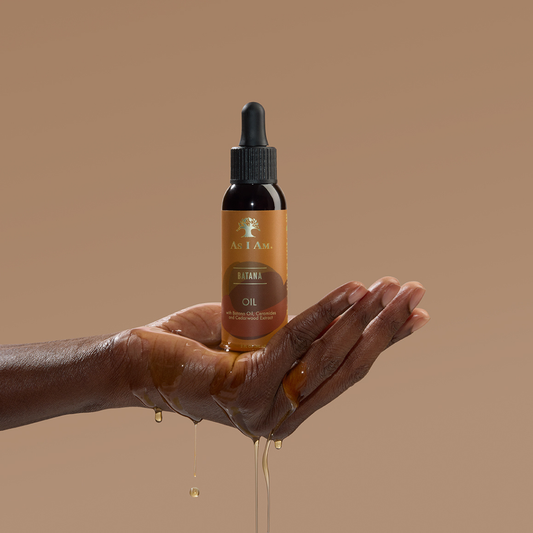 Bottle of batana Oil with oil dripping onto a hand against a brown background