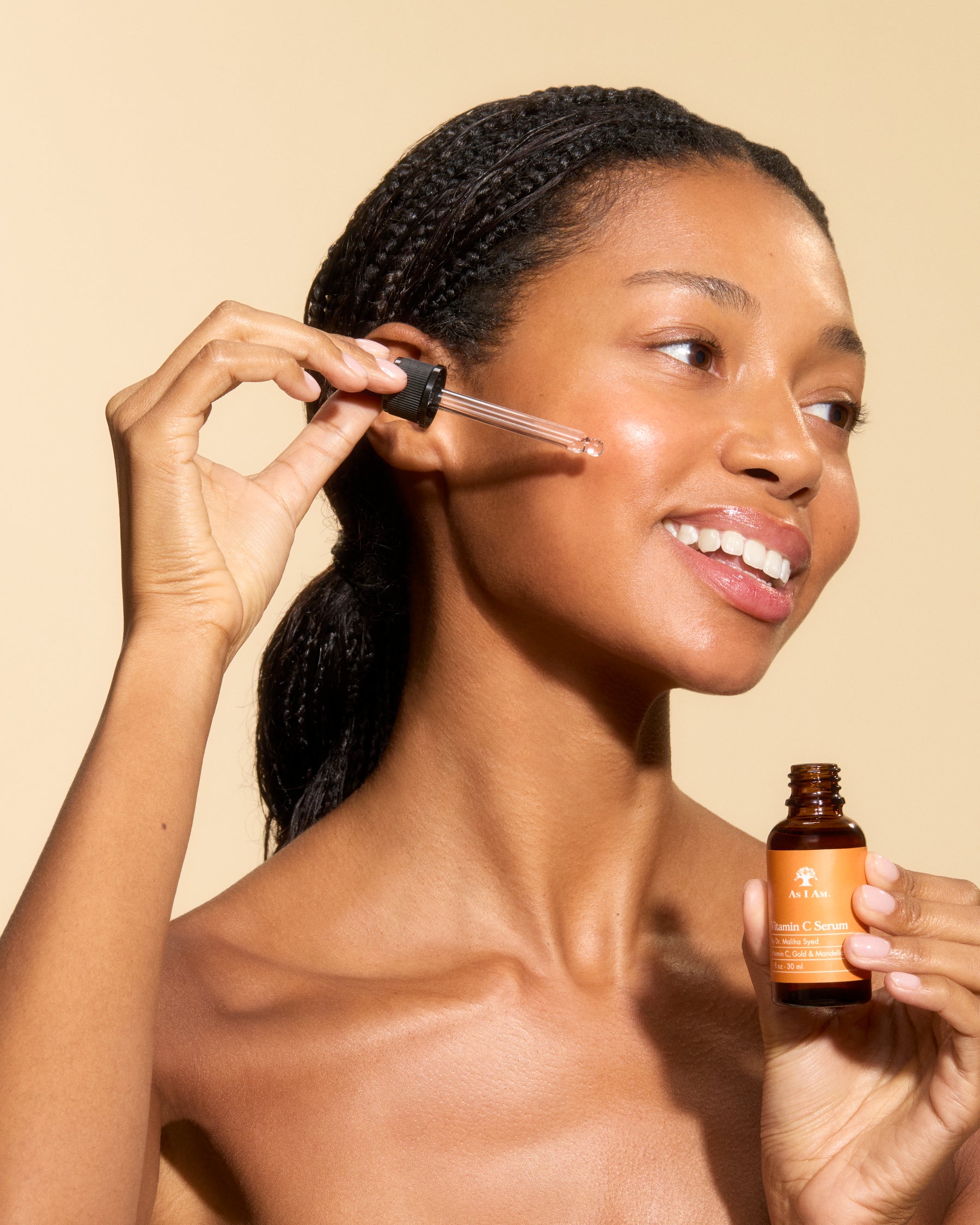 Woman applying a skincare product to her face with a dropper bottle against a beige background
