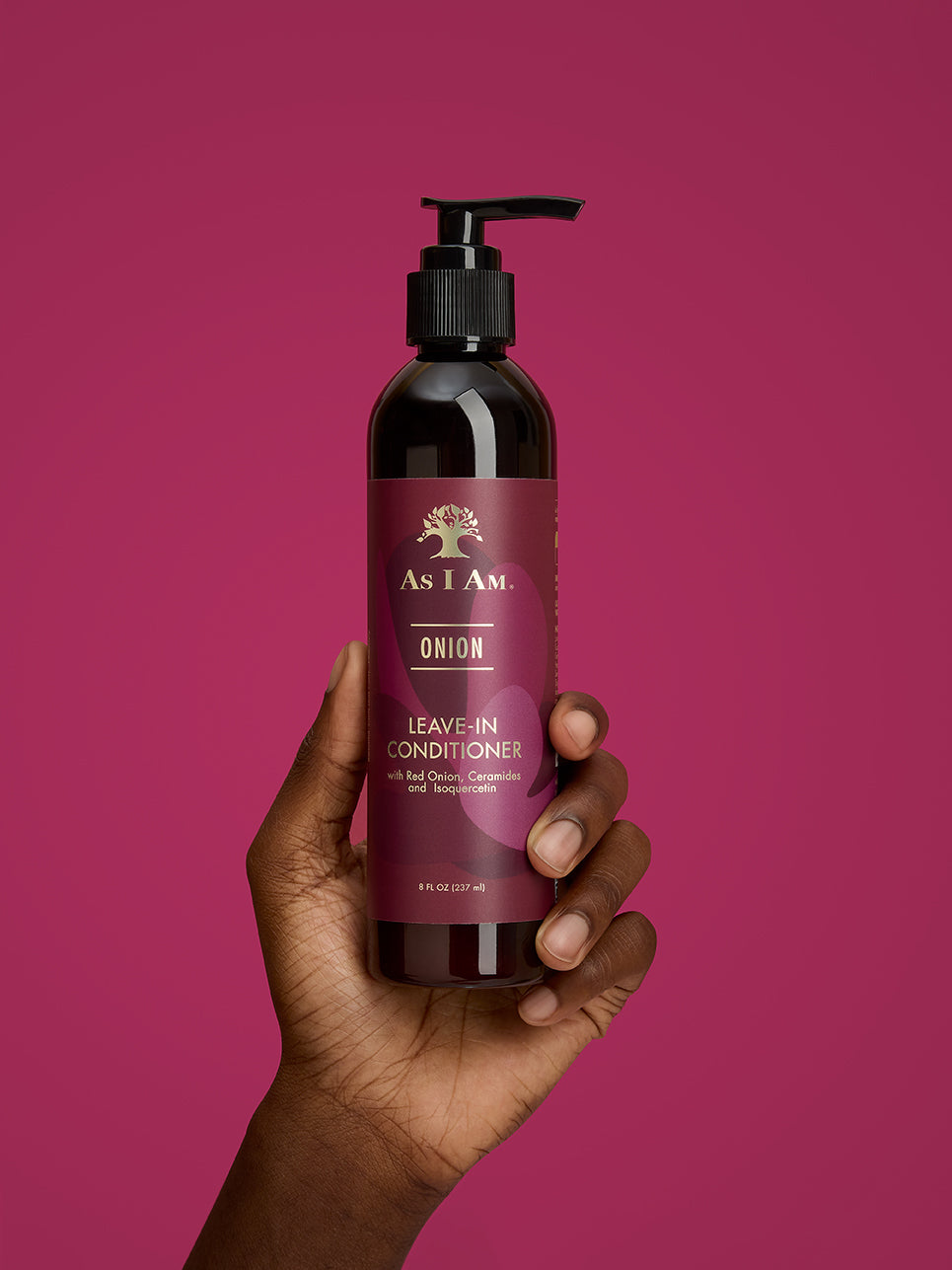 Hand holding a bottle of 'As I Am' Onion Leave-In Conditioner against a pink background
