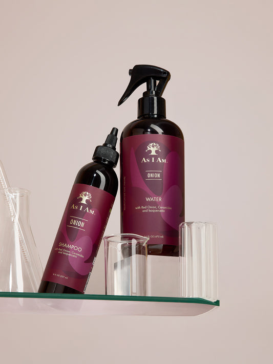 Deux flacons de produits capillaires As I Am sur une étagère en verre avec un fond neutre
