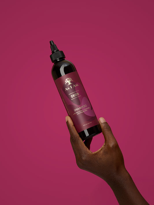Main tenant une bouteille de shampoing sur fond rose