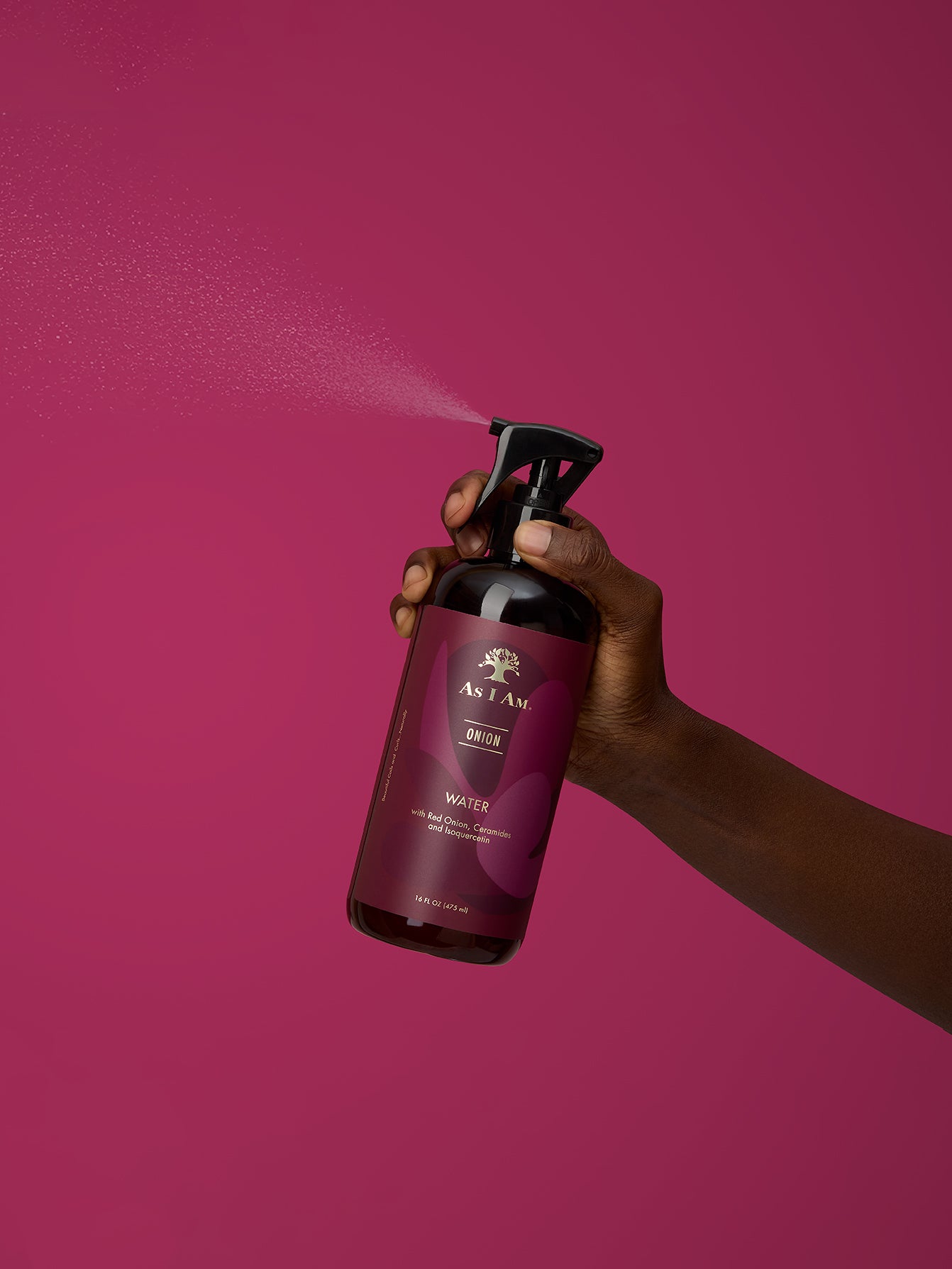 Hand holding a spray bottle labeled 'onion water' against a pink background