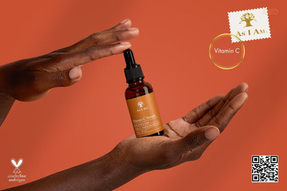 Hand holding a bottle of As I Am Vitamin C serum against an orange background